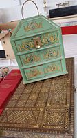Front view of the vintage lacquered wood jewelry box showing green lacquer finish with gold and blue decorative inlay, brass handle and clasp