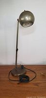 Full image showing lamp upright on wood surface with black cord coiled at base