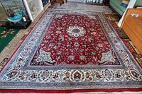 Full view of rectangular rug on floor, showing red field and ivory border