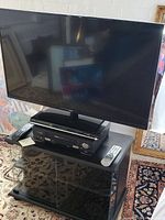 Front view of JVC 39 inch TV on top of Toshiba DVD player and RCA VCR, all on black two-tiered glass-doored TV stand.