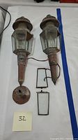 Pair of vintage copper outdoor torch lights with loose glass panels and mounting bases shown flat on a white surface