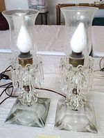 Pair of vintage electric hurricane lamps with crystal pendants and clear square bases on table.