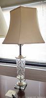 Full view of vintage lamp with fabric shade sitting on a surface in front of window blinds, showing entire lamp.