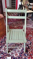 Front view of vintage painted wood folding chair with slat seat and backrest showing scratches.