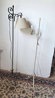 View of both vintage wrought iron floor lamps showing overall condition and style against a white wall and patterned rug.