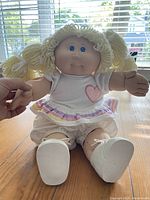 Front view of 1982 Keeley Irene Cabbage Patch doll sitting on wood table, showing original clothing and white shoes, signature on back visible