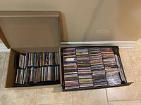 Two large boxes filled with over 200 CDs stacked and arranged with spines showing various artist names and genres.