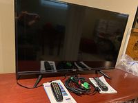 42-inch RCA LED HDTV with display off on wooden surface with remotes and cords in front