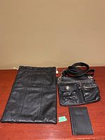 Photo showing Roots genuine black leather crossbody bag with front zippered and buttoned pockets, adjustable strap, Roots passport holder, and black leather shoe bag.