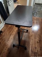 Full side view of black over bed table showing tabletop surface, vertical support and caster base.