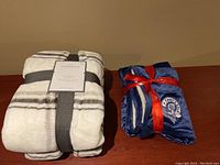 Photo showing both blankets next to each other: the white with black stripe micro plush blanket with tag and the blue and white Chief of Police Gala blanket tied with red ribbon.
