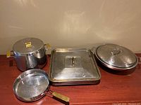 Cookware assortment displayed on surface including pot, warming pan, wok, and fry pan with lids visible