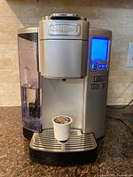 Front view of silver Cuisinart single serve coffee maker with water reservoir, LED display lit up blue, buttons, drip tray, and coffee pod on tray.