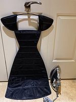 Full view of the black dress-shaped jewelry holder and Shark iron on floor.
