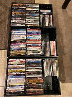 Three images showing densely packed black crates filled with close to 200 DVDs and some Blu-rays in standard cases. Movie titles visible on the spines include a wide mix of genres and titles from classics to recent releases.