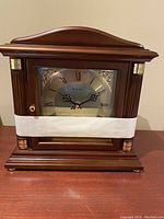 Front view of Bulova mantel clock with wood finish and gold-accented columns, clock face shows Bulova brand and Roman numerals.