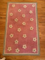 Full view of the rectangular pink wool rug with white and green floral dots and a light green border on a wooden floor.