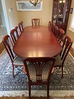 Full view of the rosewood oval dining table with 12 upholstered chairs on a patterned rug, showing the table shape and chair design.