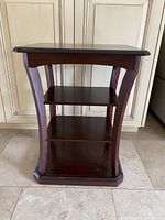 Front view of the wooden side table showing three shelves and curved legs in a dark brown finish.