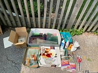 Overview of lot showing multiple boxes with assorted stained glass pieces in various colors, some tools and bottles, arranged outdoors on pavement.
