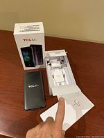 TCL 10 Pro phone with open box showing charger, USB-C cable, SIM ejector tool and paperwork laid out on table