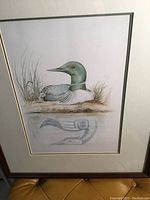 Photo of the framed Sue Coleman print showing the loon with indigenous art style reflection and surrounding grass.