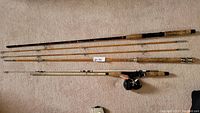 Full view of three fishing rods, showing cork handles, one with attached reel, laid out horizontally.