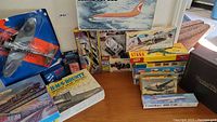 Photo showing a variety of boxed vintage model kits including airplanes, a ship, and automobiles stacked on a table.
