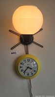 Front view of clock and light fixture mounted on wall; the light is lit, showing round white globe and yellow clock