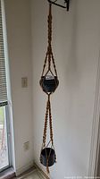 Full-length view of vintage double macrame hanger holding two black pots, showing braided hook and detailed cord work.