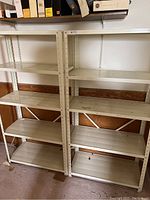Two beige metal shelving units side by side, four shelves each, showing overall condition and size.