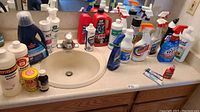 Overview of cleaning supplies arranged around a bathroom sink, showing variety and quantities.