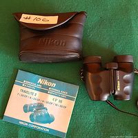 Photo showing Nikon binoculars, Nikon carrying case, and Nikon Travelite III manual on green surface.