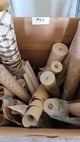 Top-down photo showing multiple rolls of vintage ready-pasted decorative vinyl sheets with various colors and patterns inside a cardboard box.