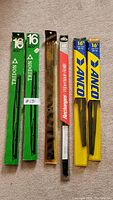 Six windshield wiper blades in original packaging displayed on carpet, from 15 to 18 inches, various brands
