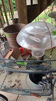 Bird feeder, metal bucket, gardening tools in blue sprinkle can bucket, and decorative birdhouse on metal shelving outdoors