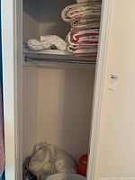 Closet with stacked folded quilts and blankets, plastic bags with textile items at the bottom.