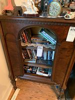 Front view showing detailed carved top trim, arched glass door, and interior shelving with various DVDs stored inside