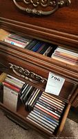 Open drawer of wooden chest filled with assorted music CDs in jewel cases, showing different titles and colors.