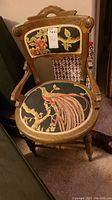 Front view of wood framed chair showing carved wood frame and needlepoint seat/back with bird and floral patterns.