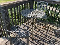 Three metal chairs arranged around a metal round bistro table with latticework top on wood deck
