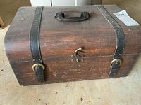 Wooden chest top view showing handle, black straps and lock with wear marks.