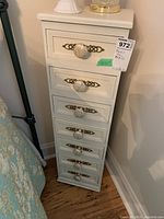 Full view of the white tower chest of drawers next to a bed, showing all seven drawers and clear glass knobs with brass backplates.