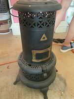 Front and side view of black vintage coal stove showing decorative cutouts and legs.