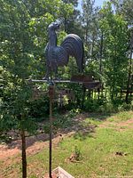 Outdoor photo showing tall black metal weather vane with rooster silhouette and directional compass.