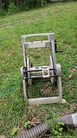 Front view of weathered plastic Suncast hose reel with hand crank on grassy ground.