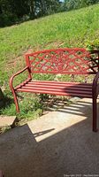 Side view of red metal bench showing armrest and slatted seat