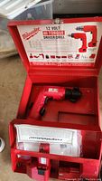 Red metal carrying case open showing Milwaukee 12 Volt Hi-Torque driver/drill inside with instruction manual included.