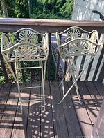 Two weathered metal basket style plant stands on a wooden deck, showing full front view of the decorative tops and legs.