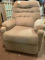 Full front view of beige upholstered recliner chair with tufted backrest and padded armrests, showing overall condition including visible stains and fabric texture.